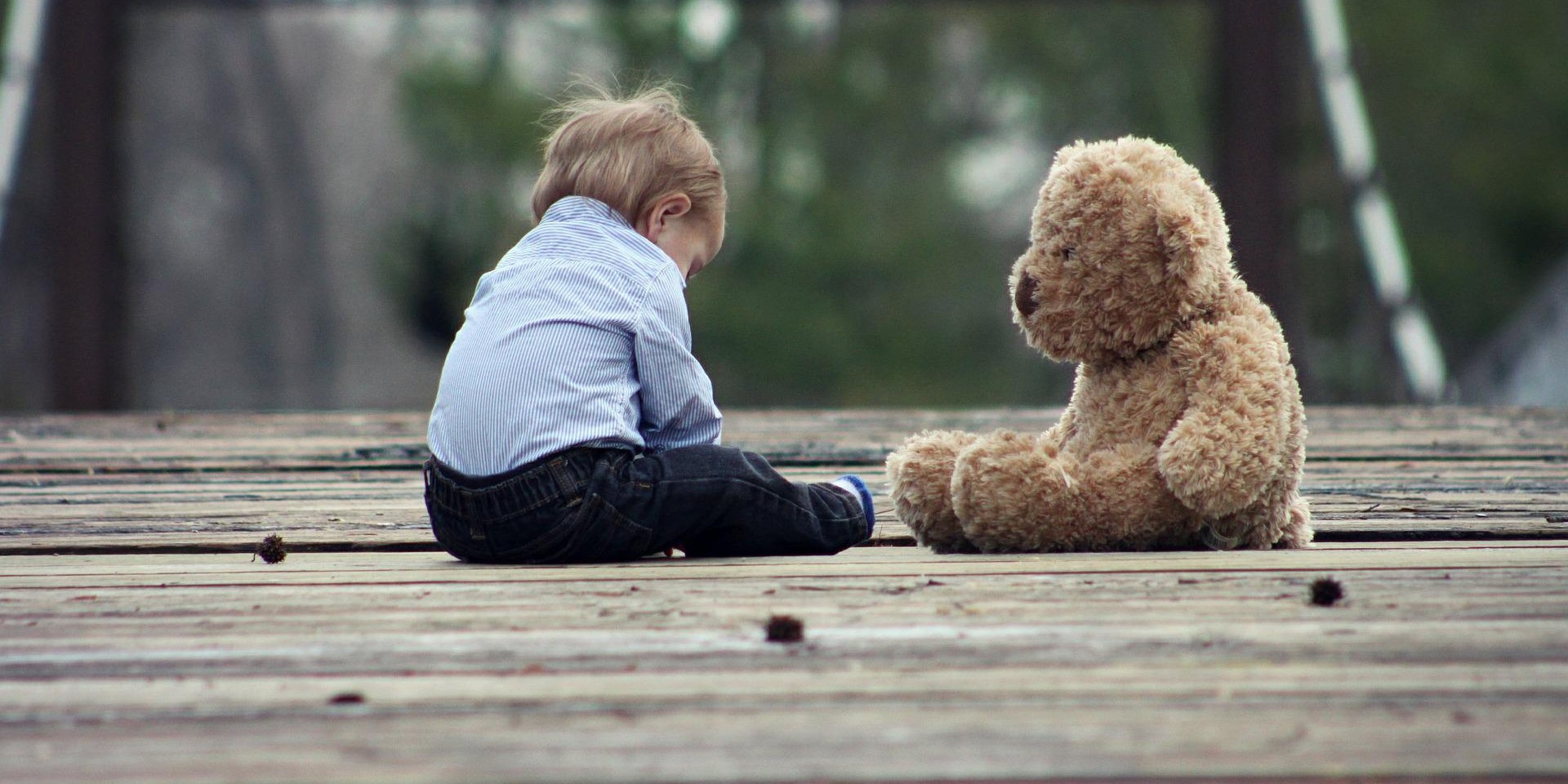 Kleiner Junge sitzt mit Teddybär auf Holzsteg